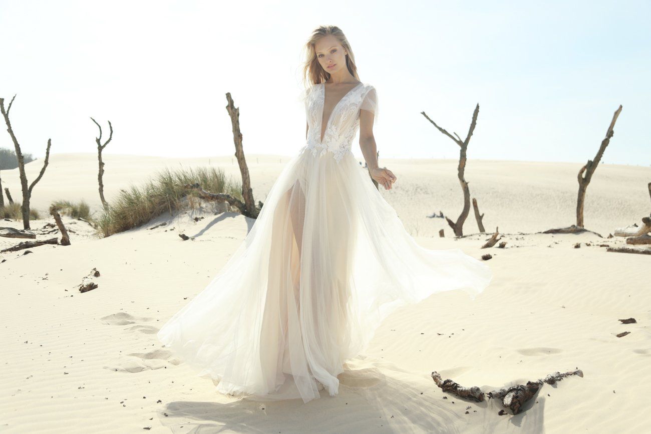 Eine Frau in einem Brautkleid steht an einem Sandstrand.