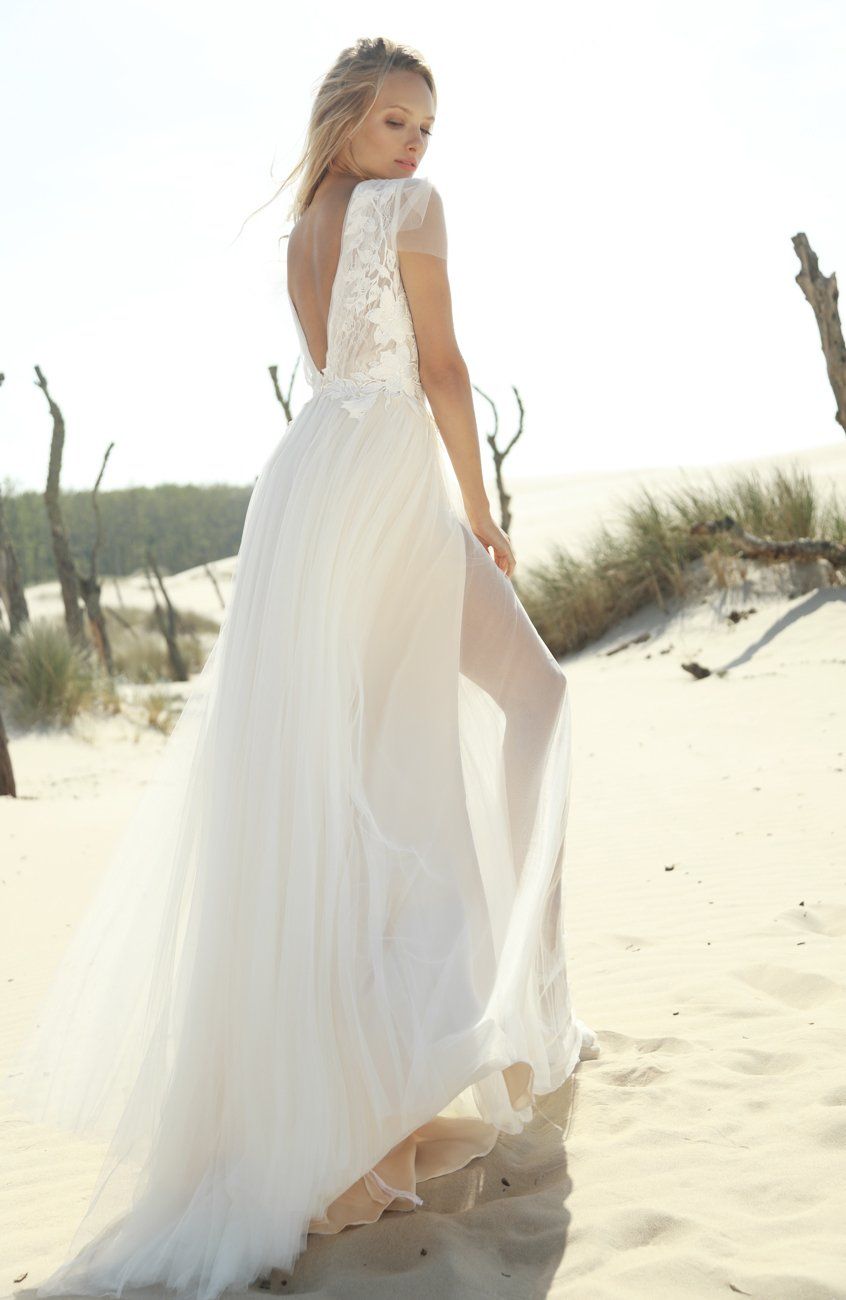 Eine Frau in einem weißen Brautkleid steht an einem Sandstrand.