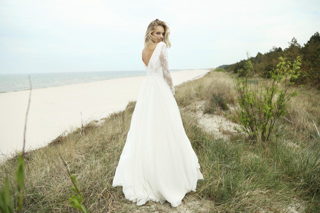 Eine Frau in einem Brautkleid steht auf einem Feld in der Nähe des Strandes.