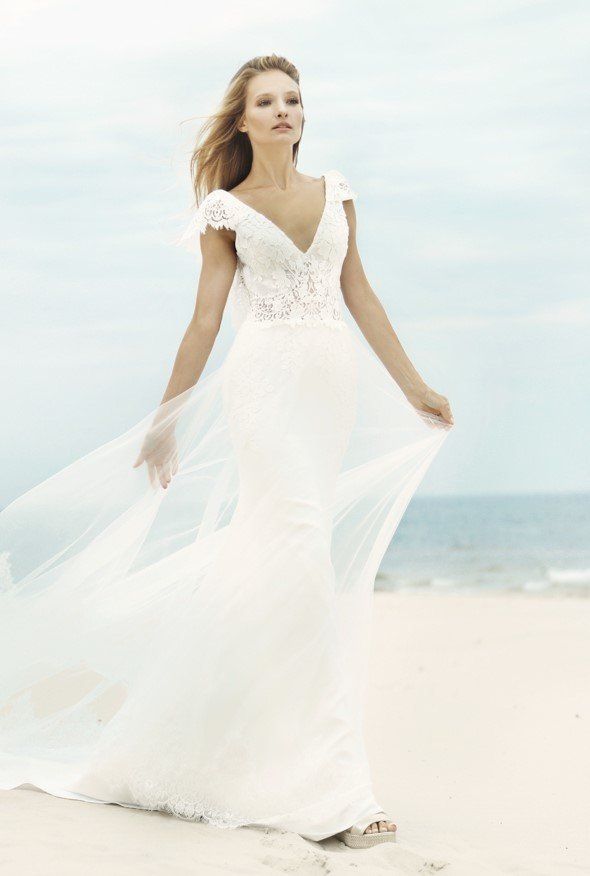 Eine Frau in einem weißen Brautkleid steht an einem Strand.