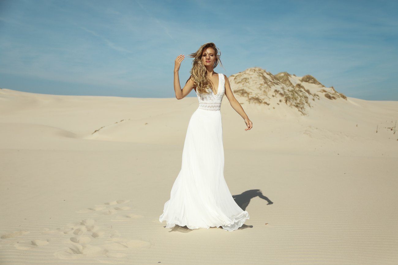 Eine Frau in einem weißen Kleid steht mitten in einer Wüste.