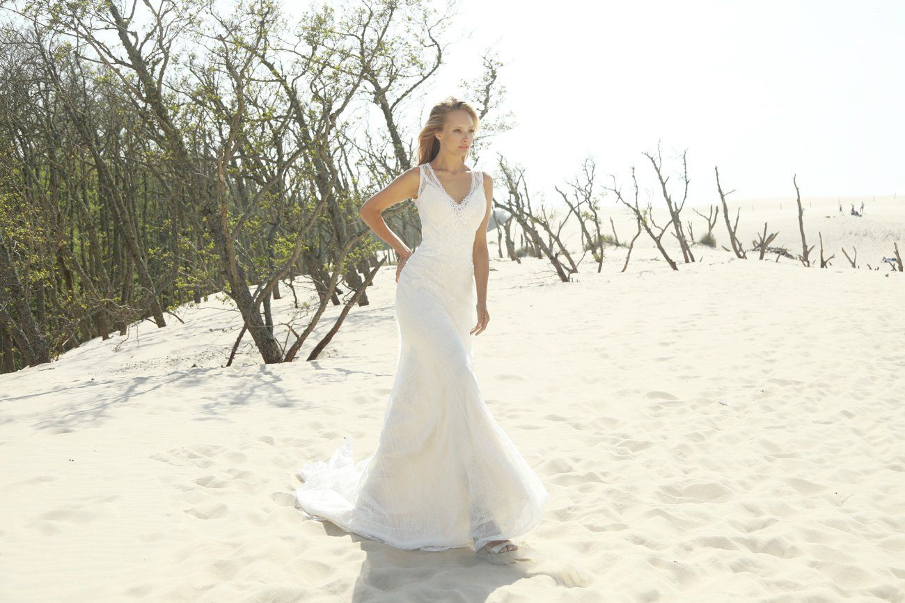 Eine Frau in einem Brautkleid steht an einem Sandstrand.
