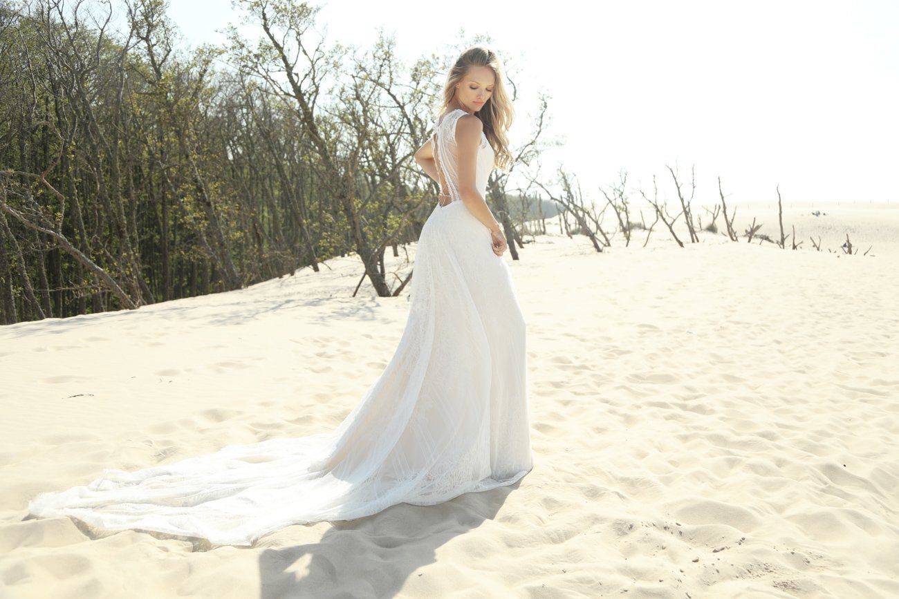 Eine Frau in einem Brautkleid steht im Sand an einem Strand.