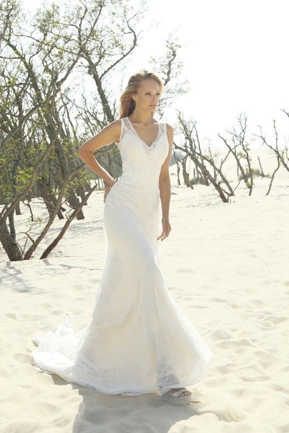 Eine Frau in einem weißen Brautkleid steht an einem Sandstrand.