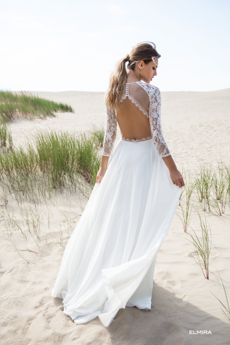 Eine Frau in einem weißen Brautkleid steht im Sand.