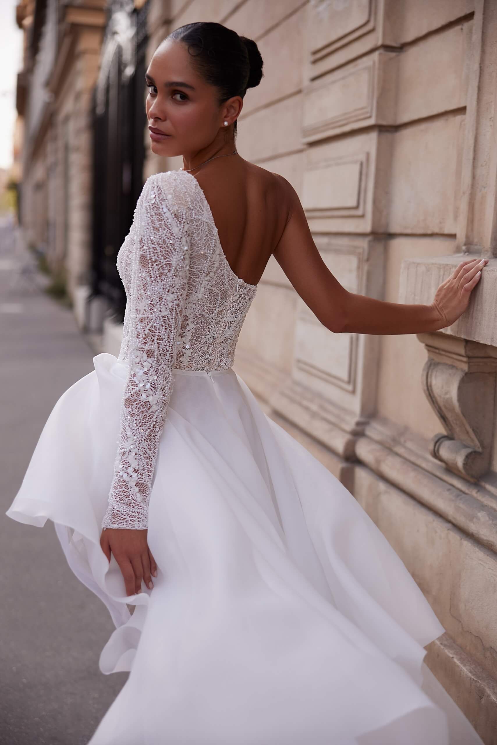 Eine Frau in einem weißen Kleid lehnt an einer Wand.