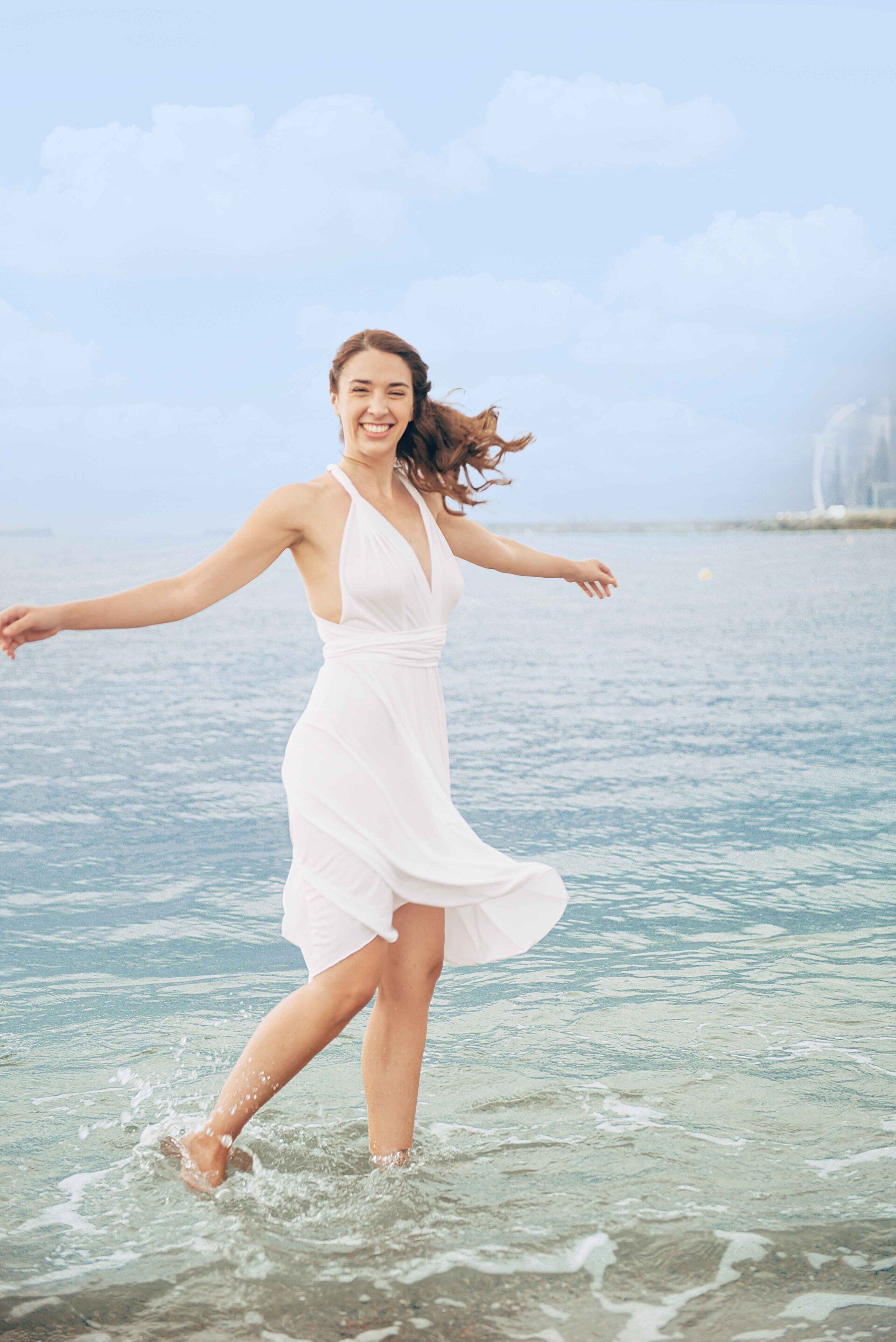 Eine Frau in einem weißen Kleid geht im Meer spazieren.