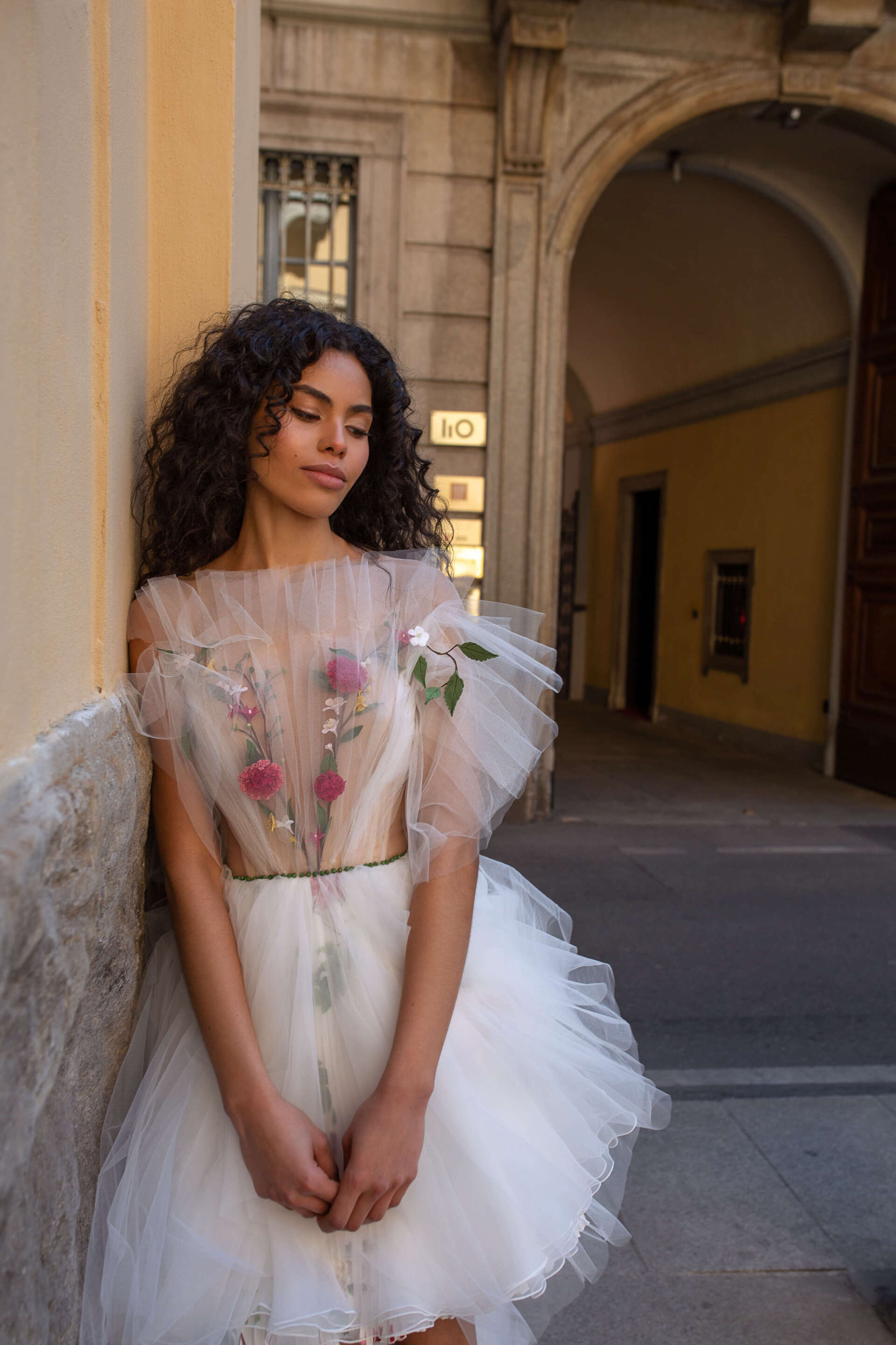 Eine Frau in einem weißen Kleid lehnt an einer Wand.