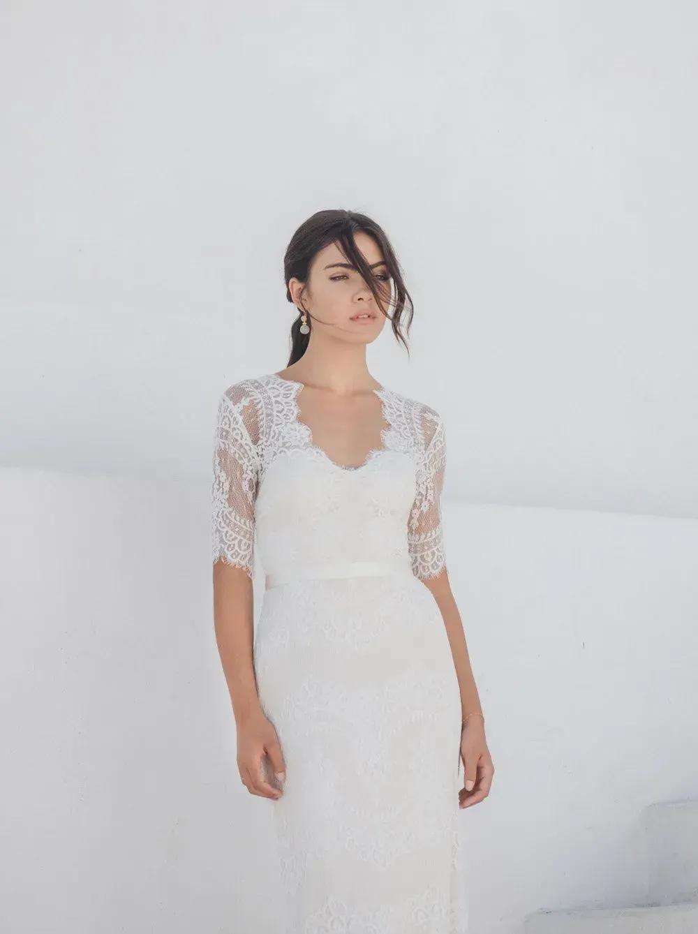 Eine Frau in einem weißen Kleid steht vor einer weißen Wand.