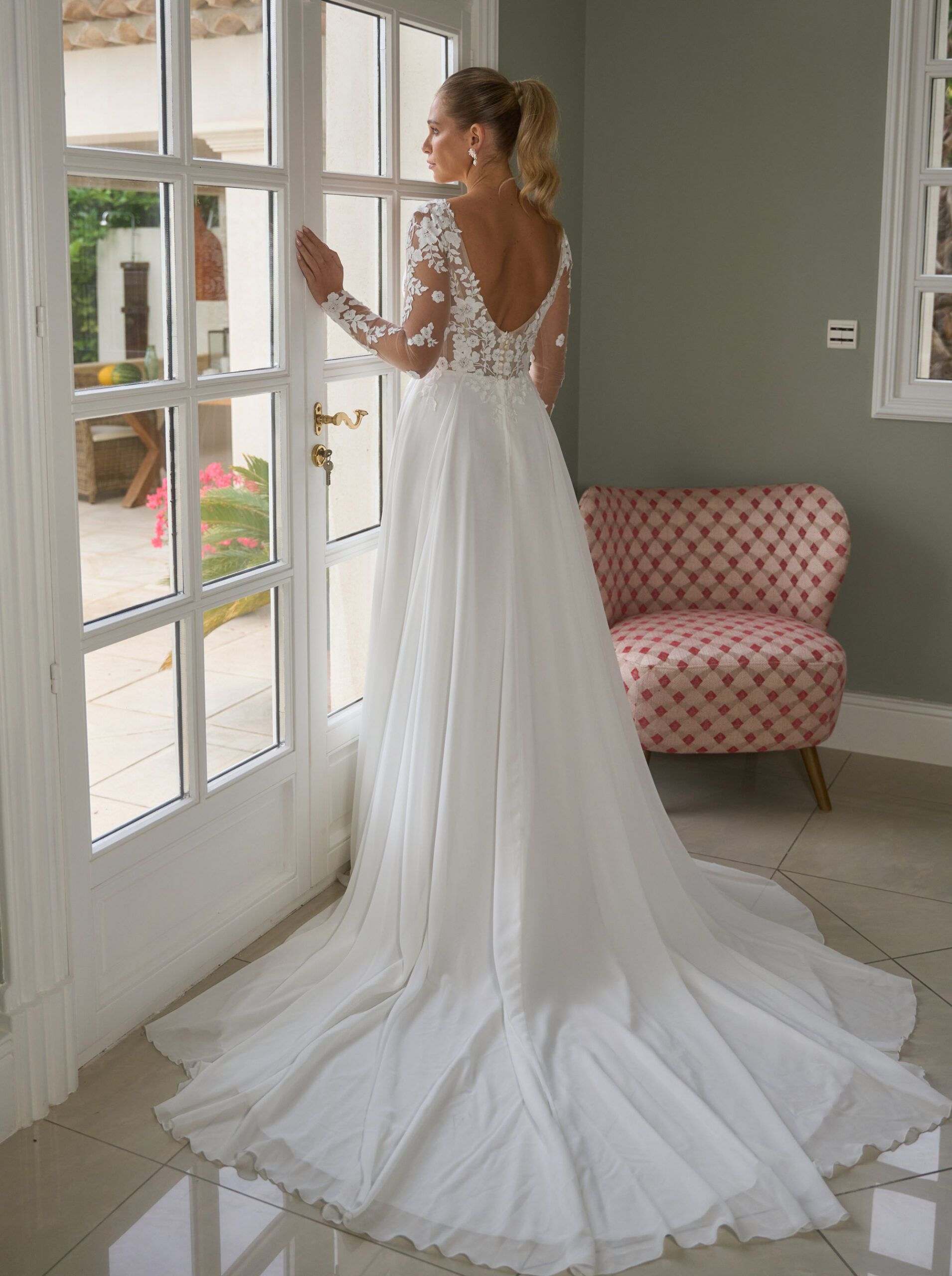 Eine Frau in einem weißen Brautkleid steht vor einem Fenster.