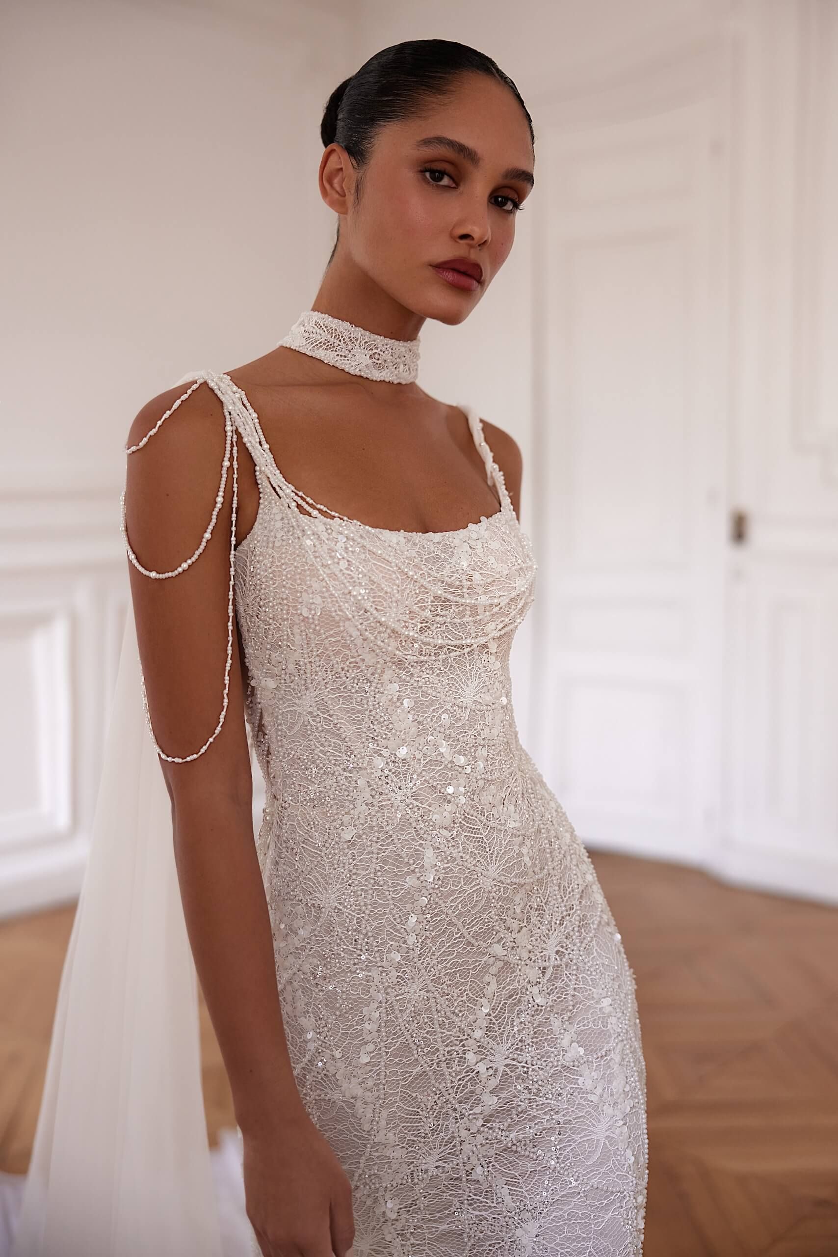 Eine Frau in einem weißen Kleid und einer Halskette steht in einem Raum.