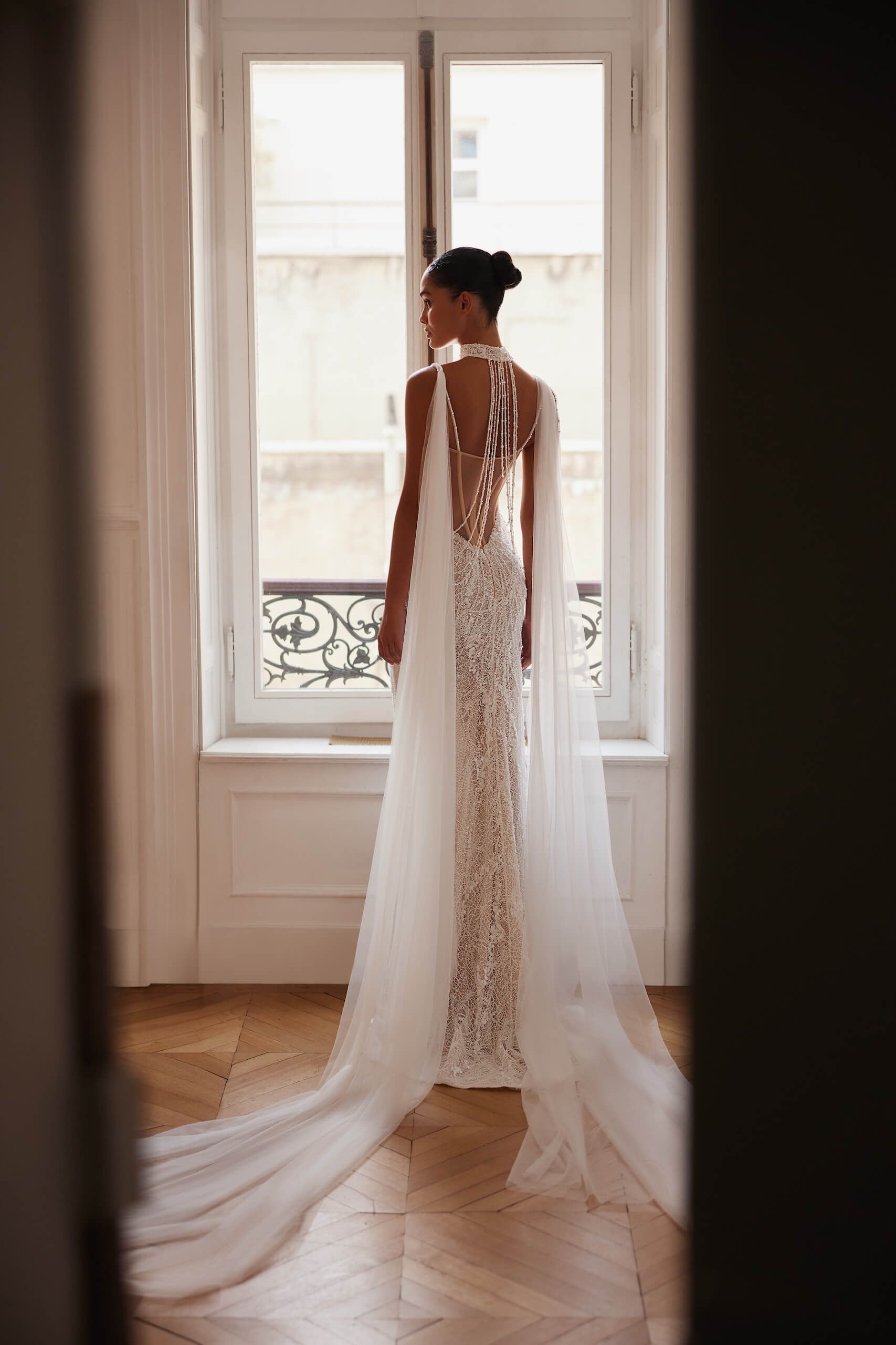Eine Frau in einem Brautkleid steht vor einem Fenster.