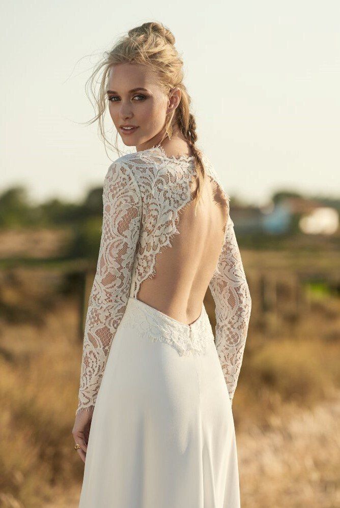 Eine Frau in einem weißen Spitzenkleid steht auf einem Feld.