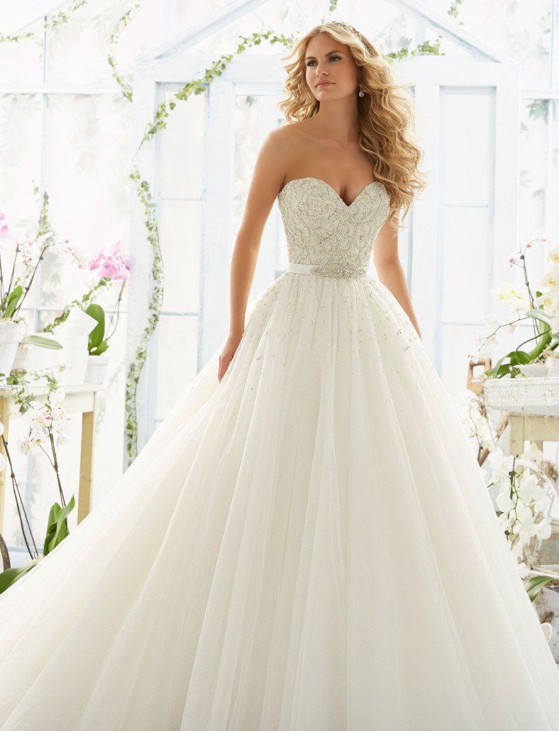 Eine Frau in einem weißen Brautkleid steht vor einem Gewächshaus.