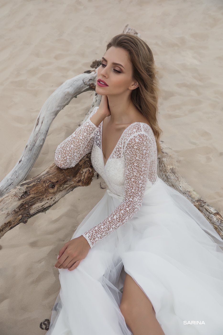 Eine Frau in einem Brautkleid sitzt auf einem Ast am Strand.