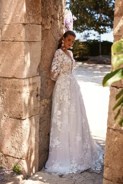 Eine Frau in einem Brautkleid lehnt an einer Steinmauer.