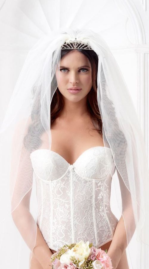 Eine Frau in einem weißen Korsett und Schleier hält einen Blumenstrauß.