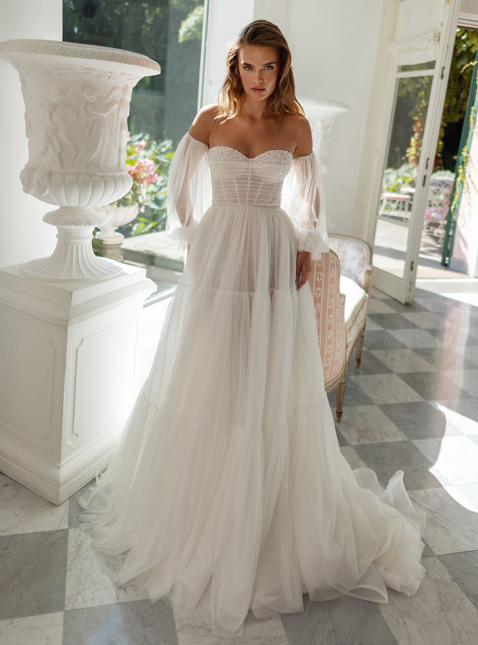 Eine Frau in einem weißen Brautkleid steht in einem Raum neben einer Vase.