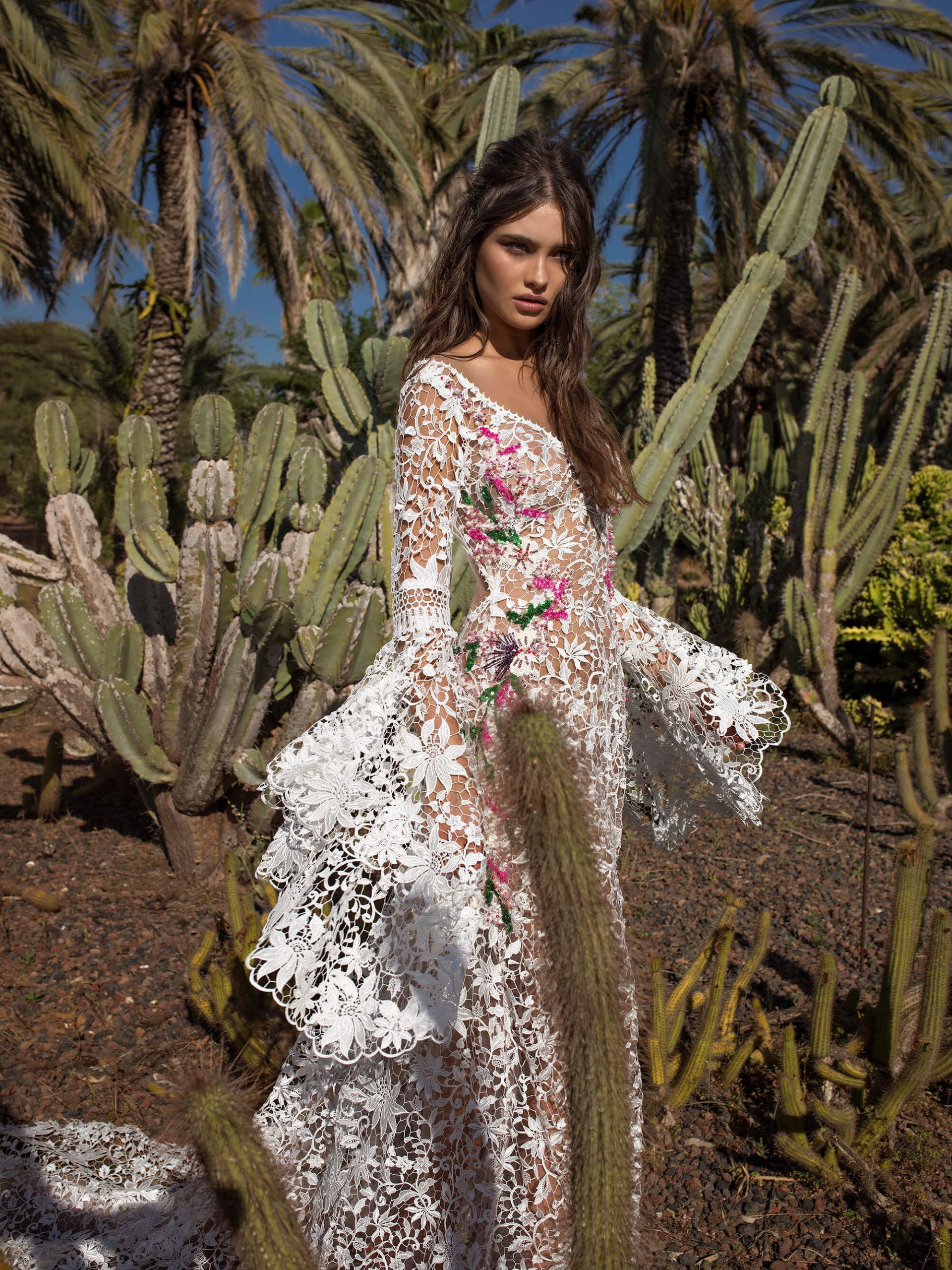 Eine Frau in einem weißen Spitzenkleid steht neben einem Kaktus.