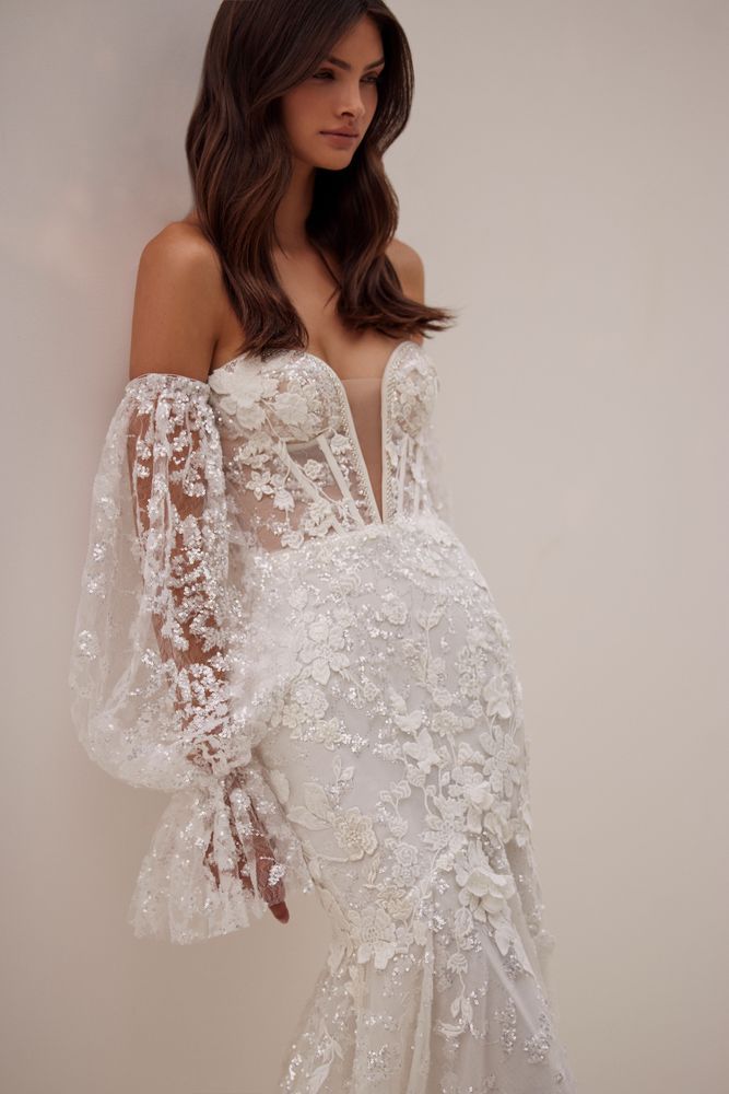 Eine Frau trägt ein weißes Spitzenbrautkleid mit langen Ärmeln.