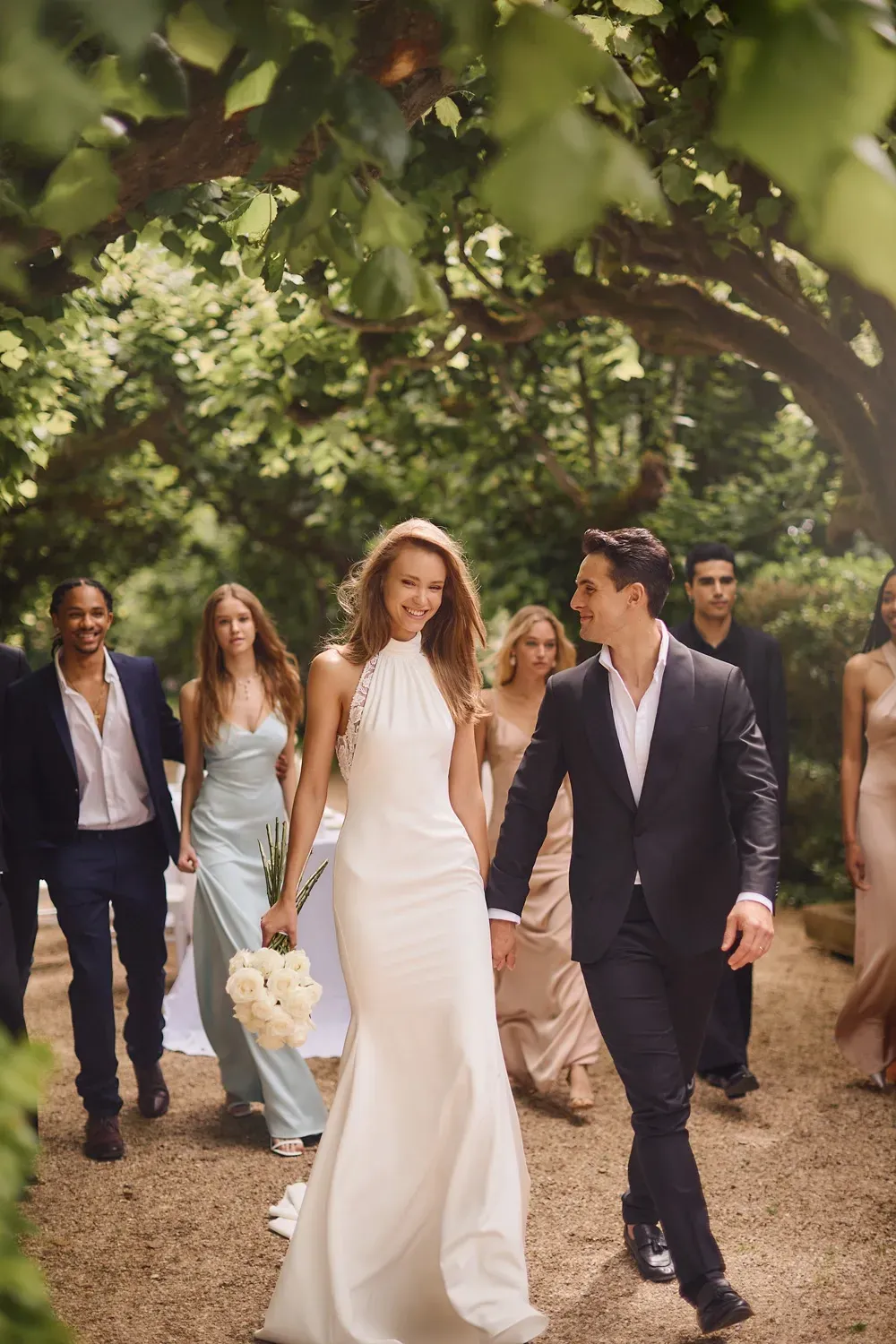 Eine Braut und ein Bräutigam gehen mit ihrer Hochzeitsgesellschaft einen Weg entlang.