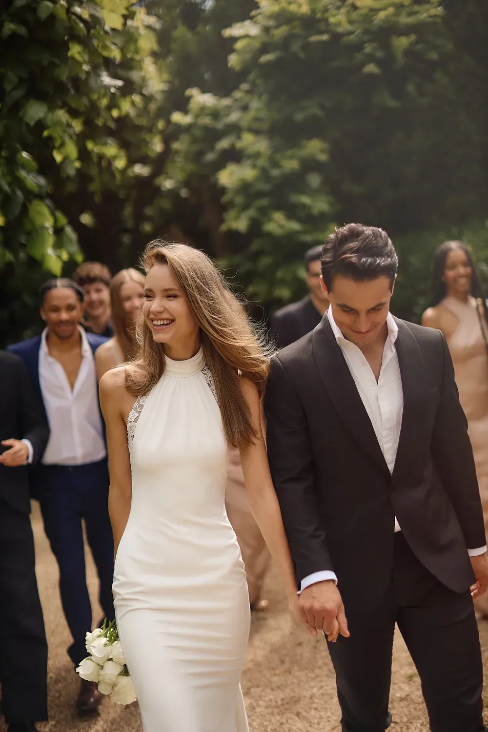 Eine Braut und ein Bräutigam gehen mit ihrer Hochzeitsgesellschaft einen Weg entlang.
