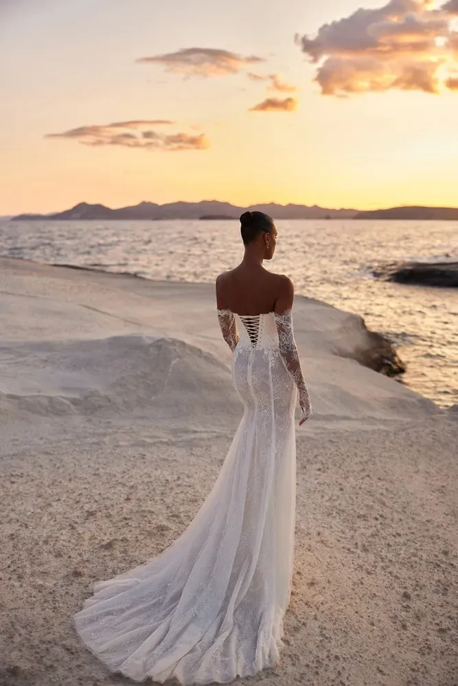 Eine Frau in einem Brautkleid steht bei Sonnenuntergang an einem Strand in der Nähe des Meeres.
