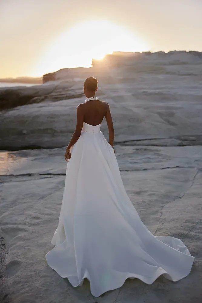 Eine Frau in einem weißen Brautkleid steht bei Sonnenuntergang an einem Strand.