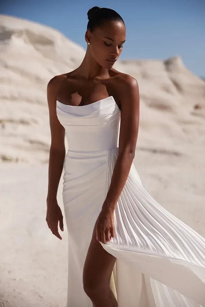 Eine Frau in einem weißen Kleid steht im Sand.