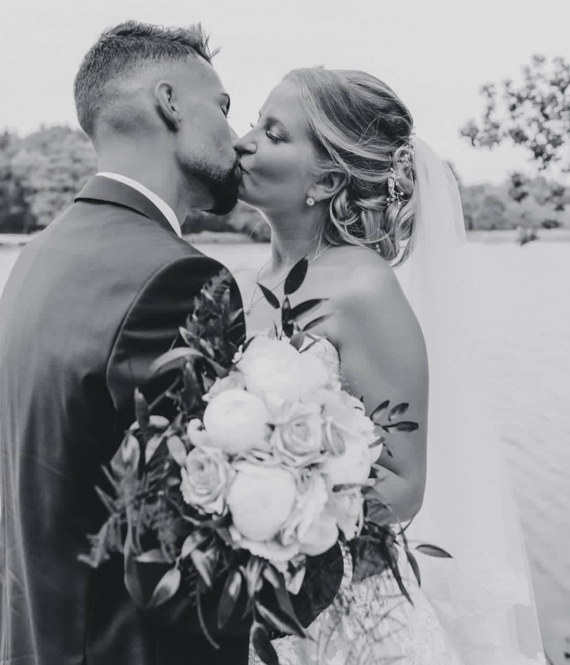 Ein Schwarzweißfoto einer Braut und eines Bräutigams, die sich an ihrem Hochzeitstag küssen.