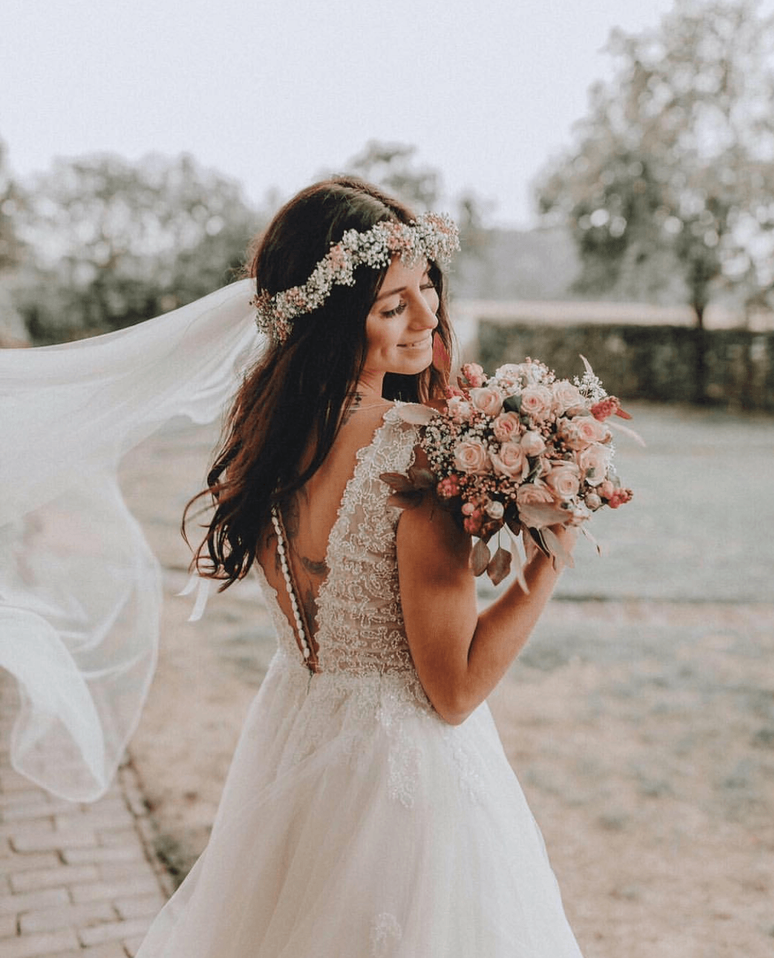 Die Braut trägt einen Blumenkranz und hält einen Blumenstrauß in der Hand.