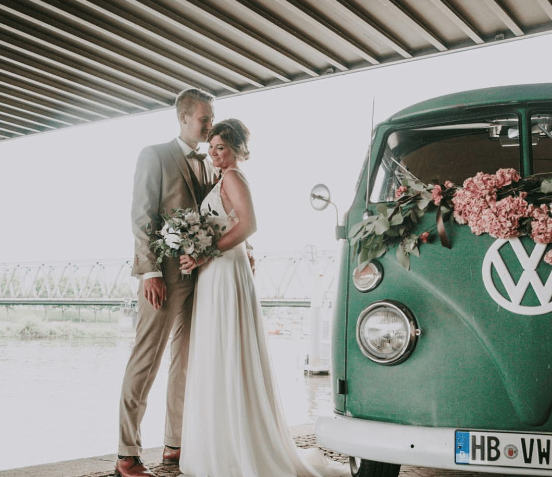 Ein Brautpaar steht vor einem grünen VW-Bus.