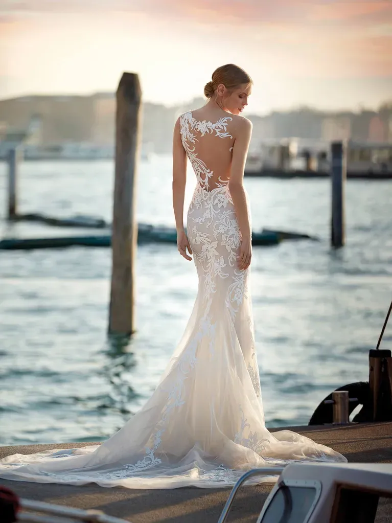 Eine Frau in einem Brautkleid steht neben einem Gewässer.