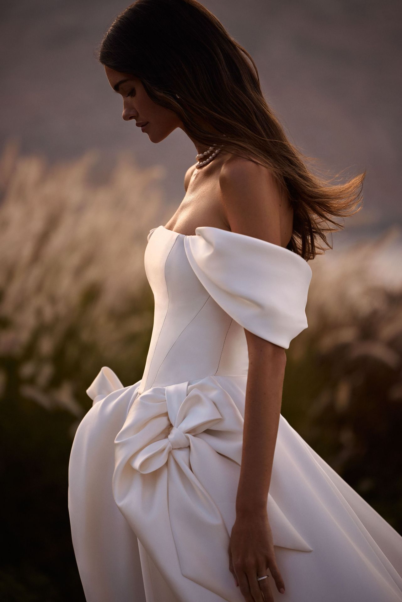 Frau in einem weißen, schulterfreien Brautkleid mit Schleife. Draußen, Feld, goldenes Licht.