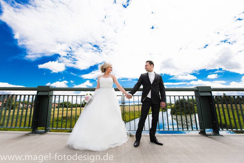 Eine Braut und ein Bräutigam stehen Händchen haltend auf einer Brücke