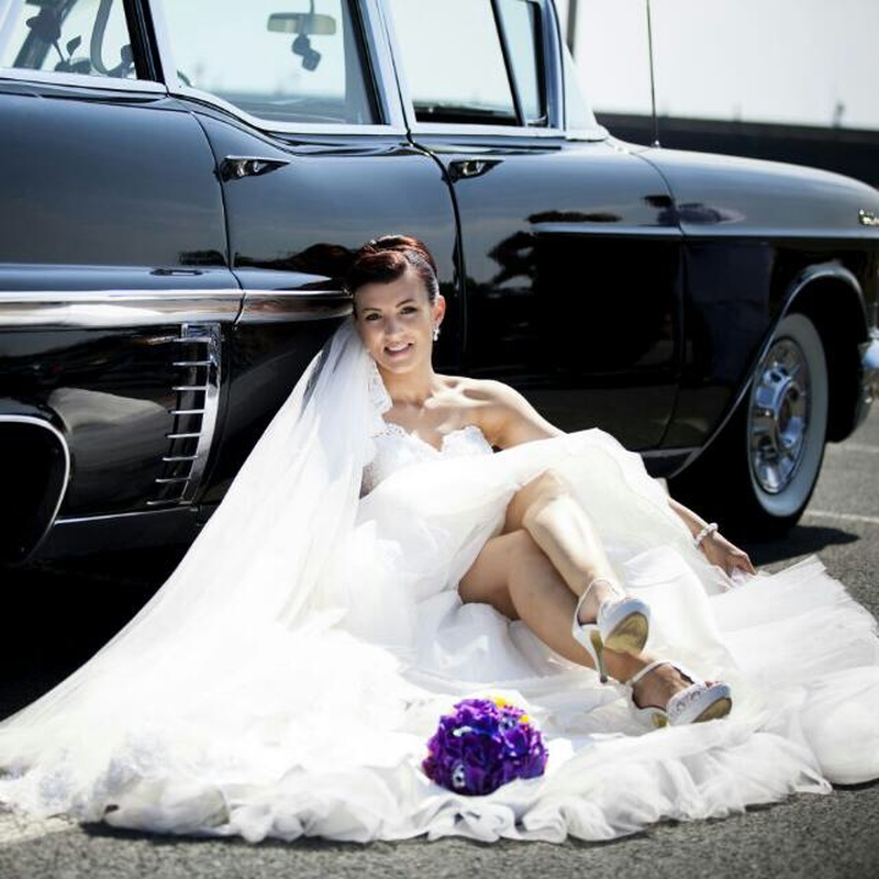 Eine Frau im Brautkleid sitzt neben einem schwarzen Auto