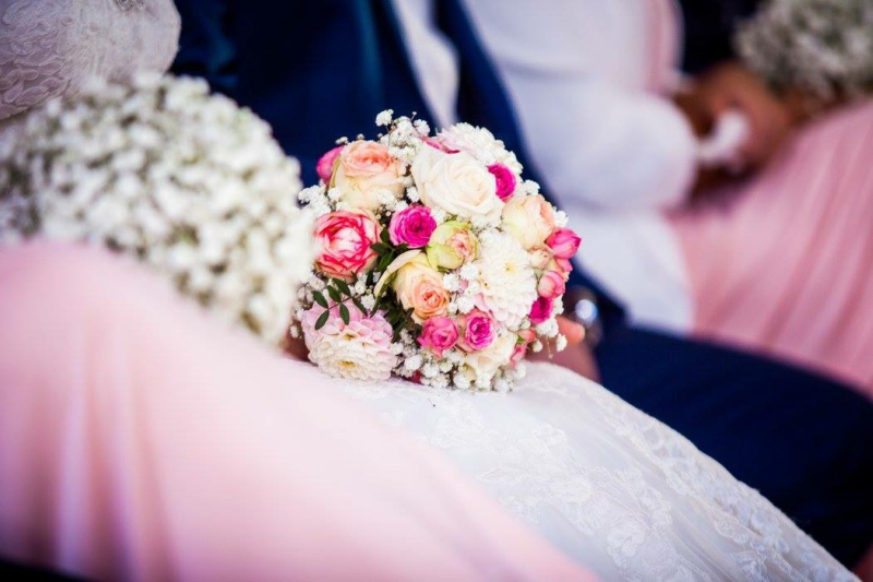 Eine Braut und ein Bräutigam sitzen nebeneinander und halten einen Blumenstrauß in der Hand.