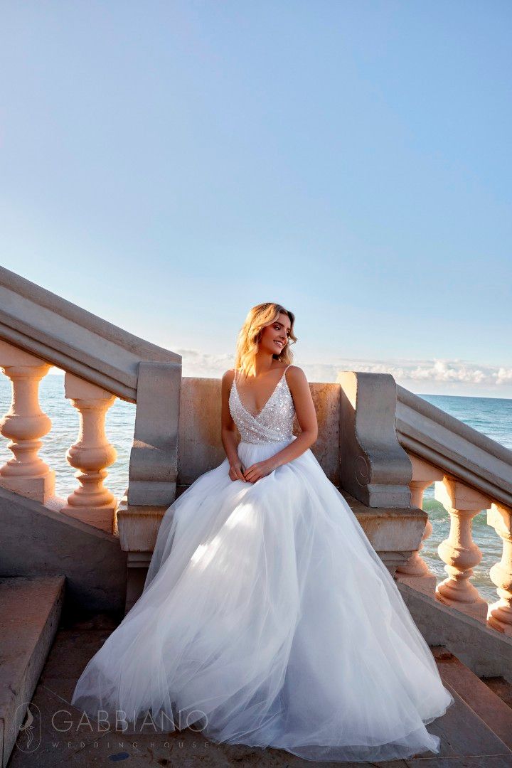 Eine Frau in einem Brautkleid sitzt auf einer Treppe am Meer.