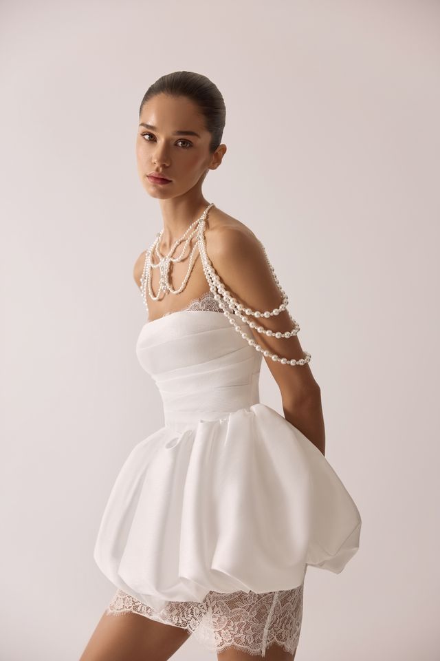 Frau in einem weißen trägerlosen Kleid mit Perlenkette, blickt in die Kamera, Studioeinstellung.