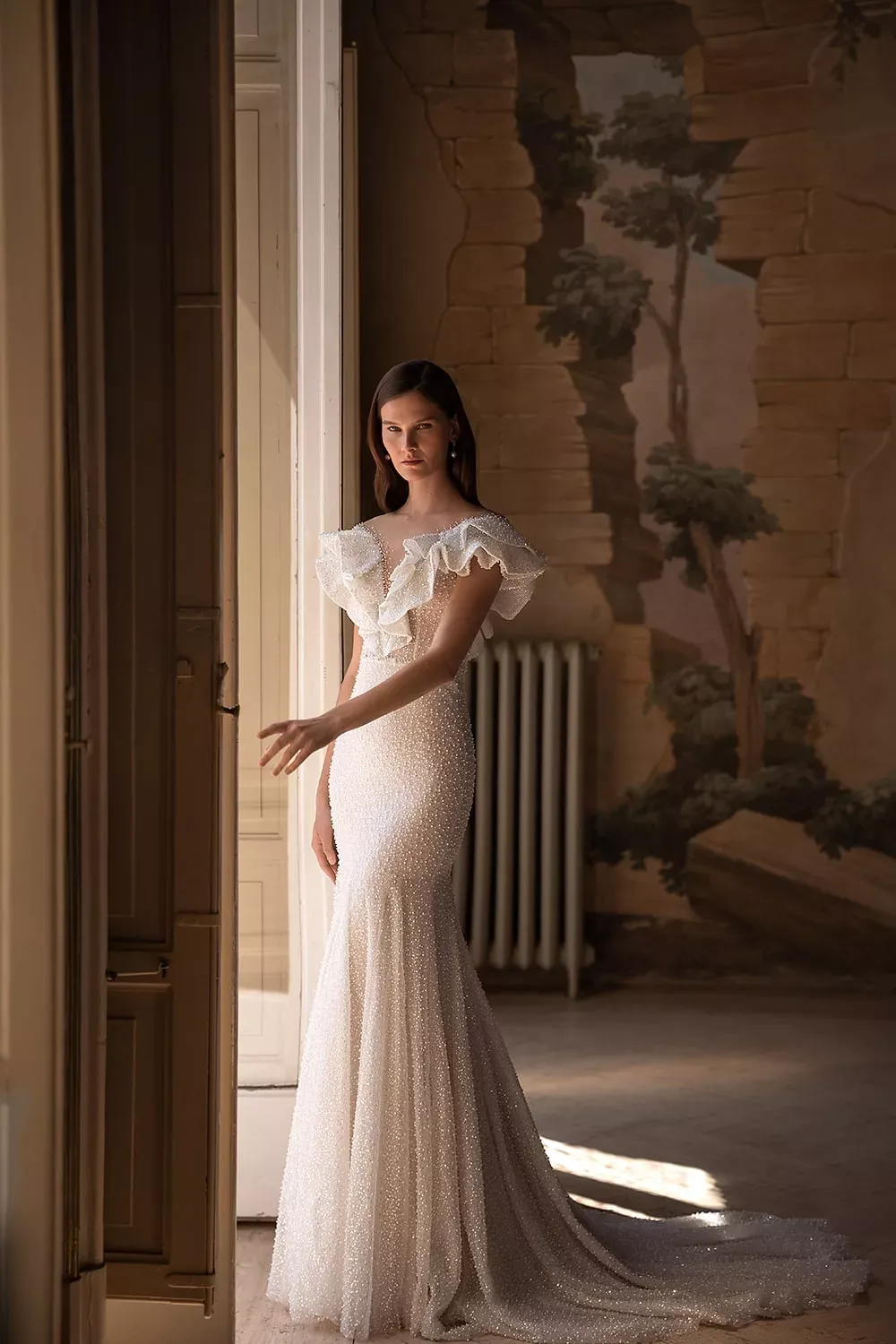 Eine Frau in einem Brautkleid steht vor einem Fenster.