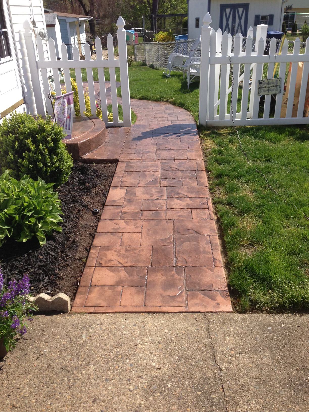 A walkway leading to a house with a white picket fence.
