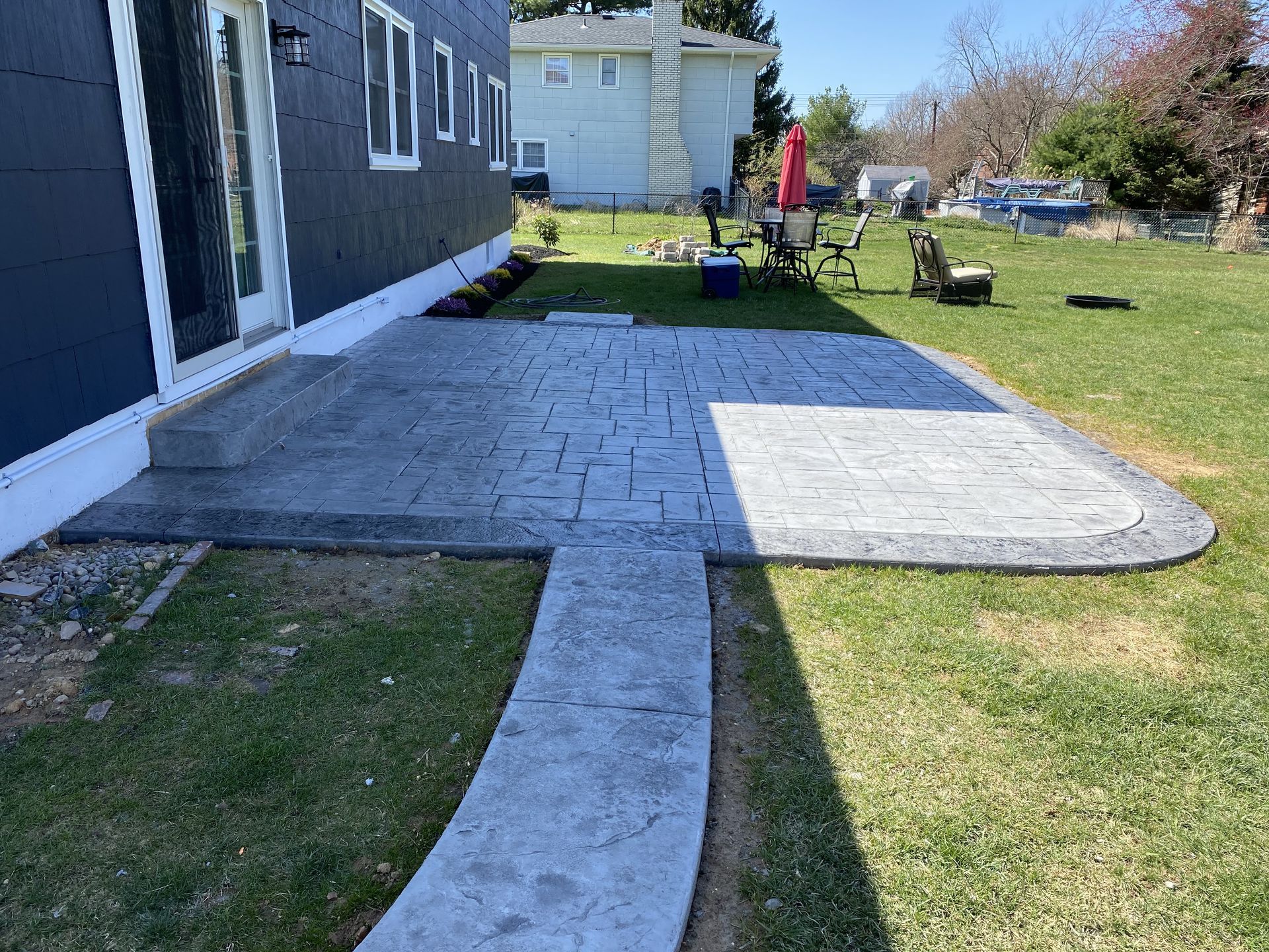 A concrete walkway leading to a patio in front of a house.