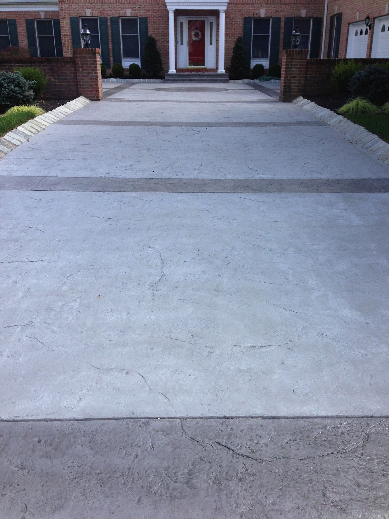 A concrete driveway leading to a brick house with a red door.