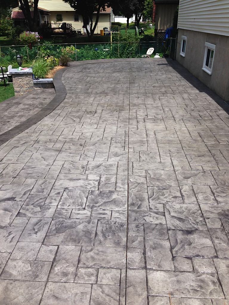 A concrete driveway leading to a house with a patio in the background.
