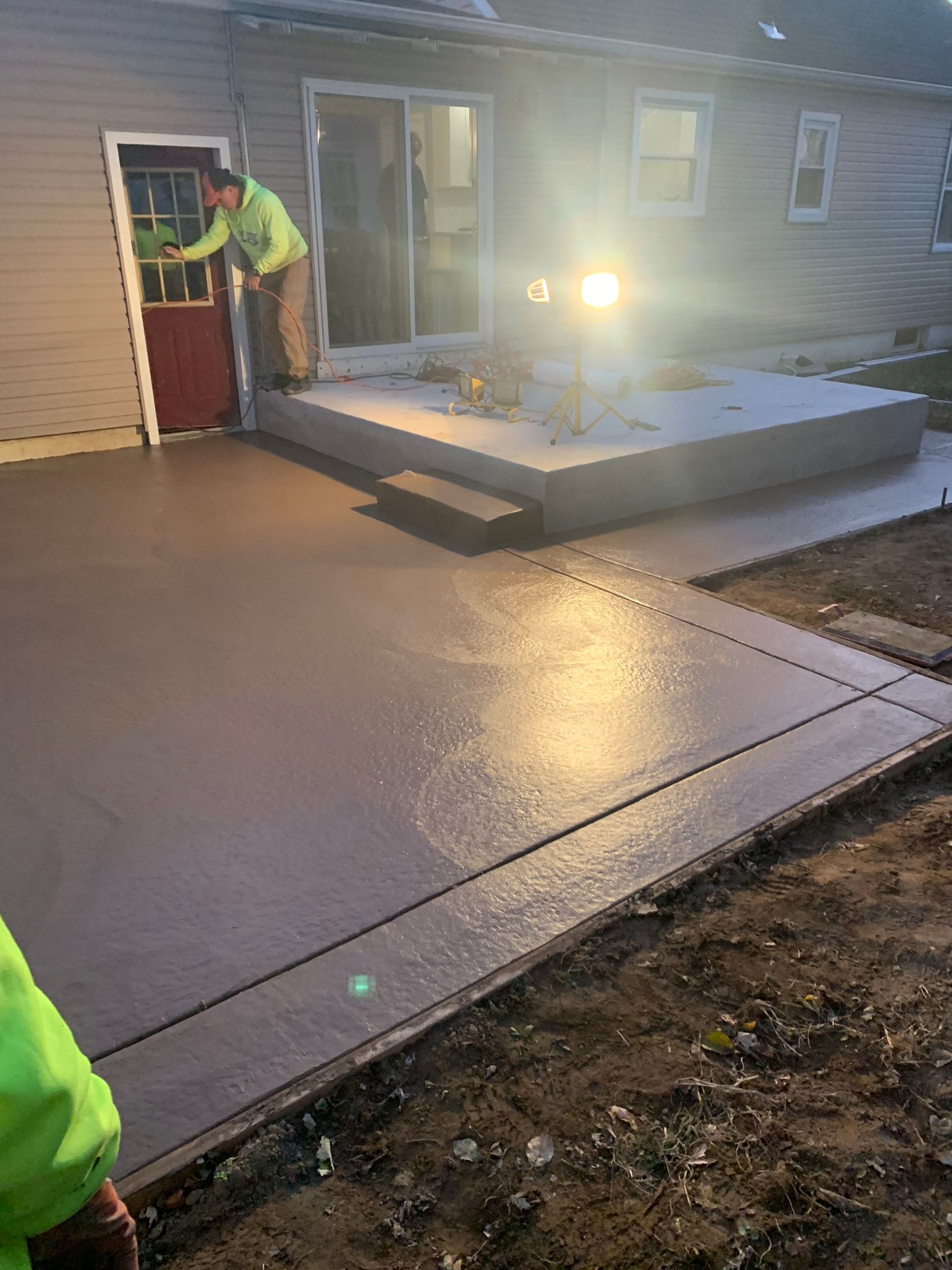 A man is working on a concrete patio in front of a house.