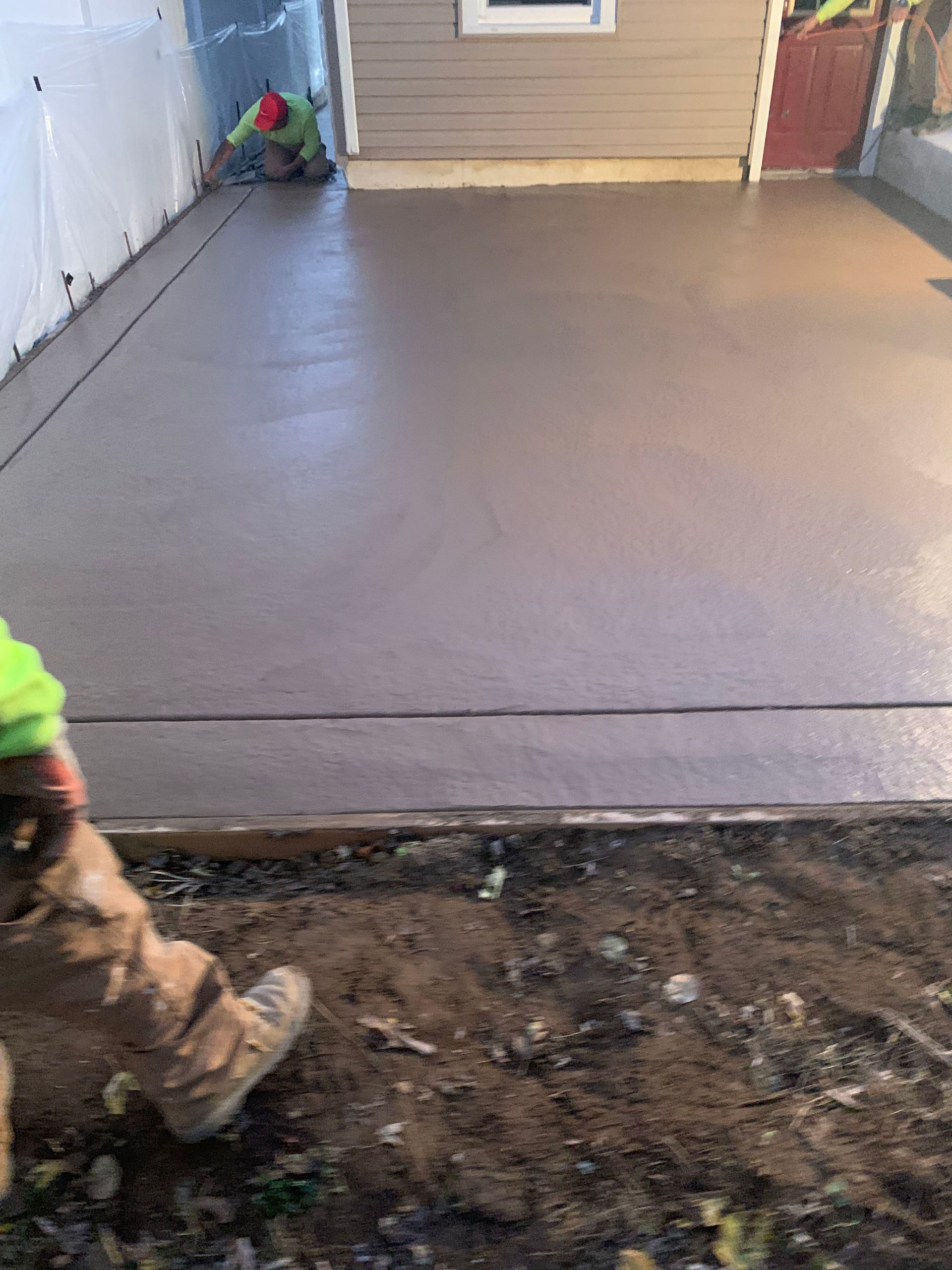 A man is working on a concrete driveway in front of a house.