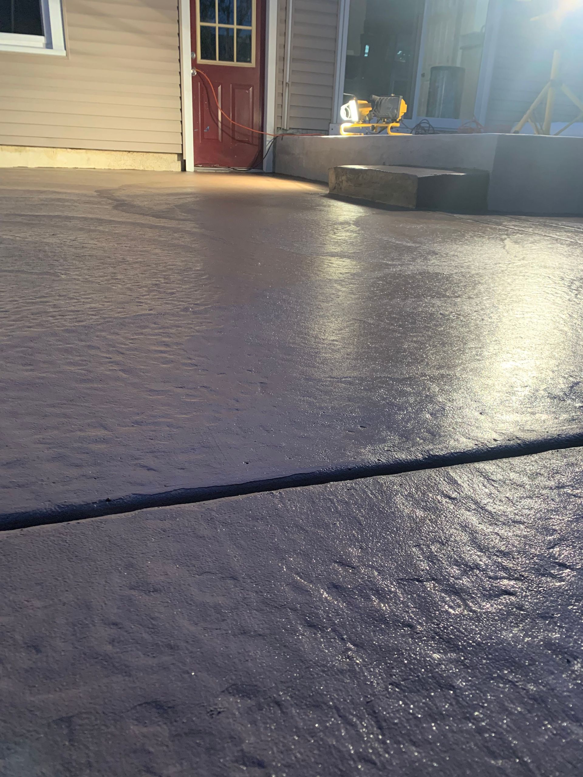 A concrete driveway in front of a house with a red door.