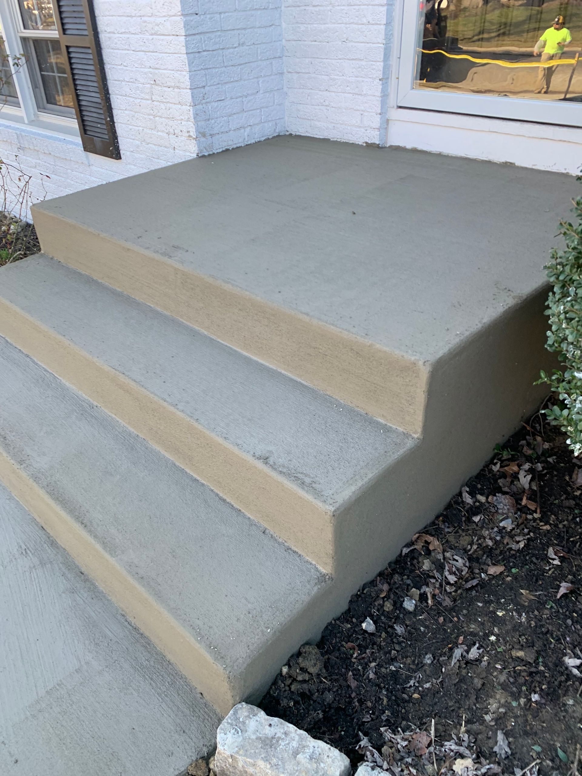 A concrete porch with steps leading up to a white brick house.