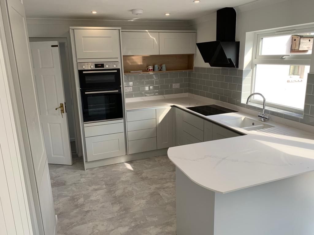 A kitchen with white cabinets , a stove , a sink , and a window.