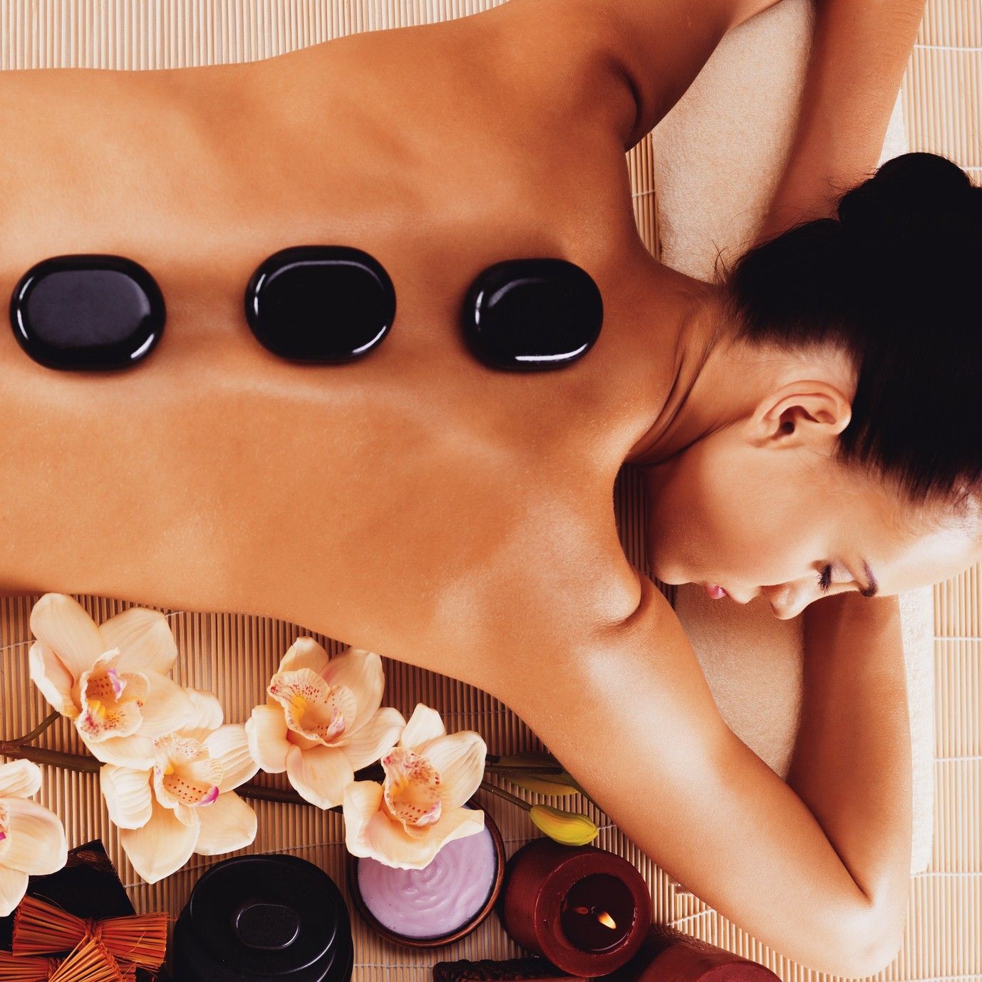 Woman receiving hot stone massage on a massage table with flowers and a candle.